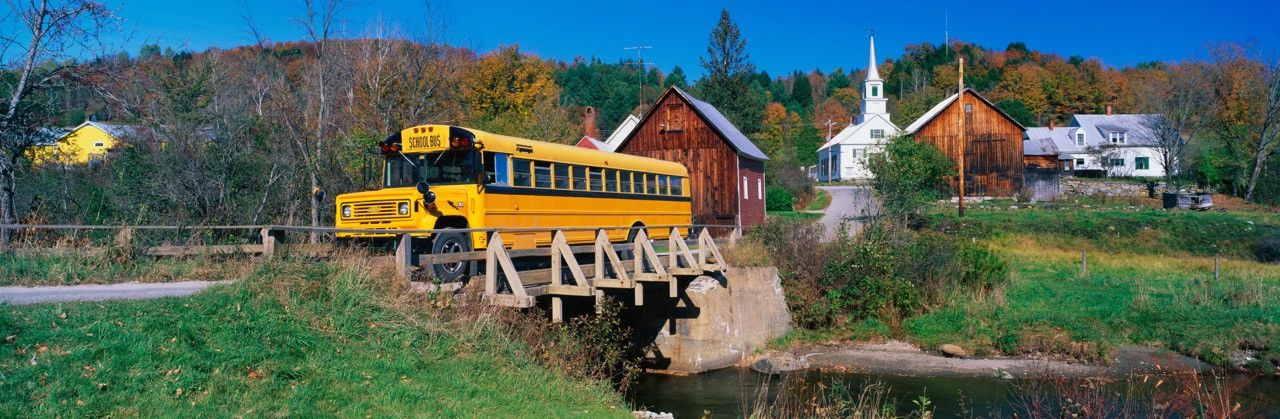 Yellow school bus crossing a bridge in a rural town.