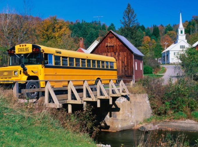 Yellow school bus crossing a bridge in a rural town.