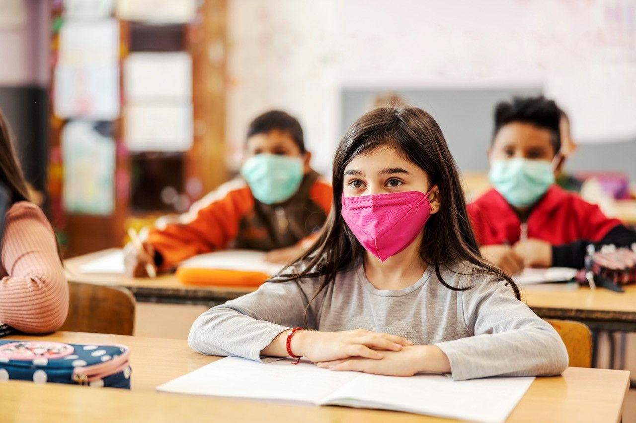 Children at desks at school wearing protective masks.