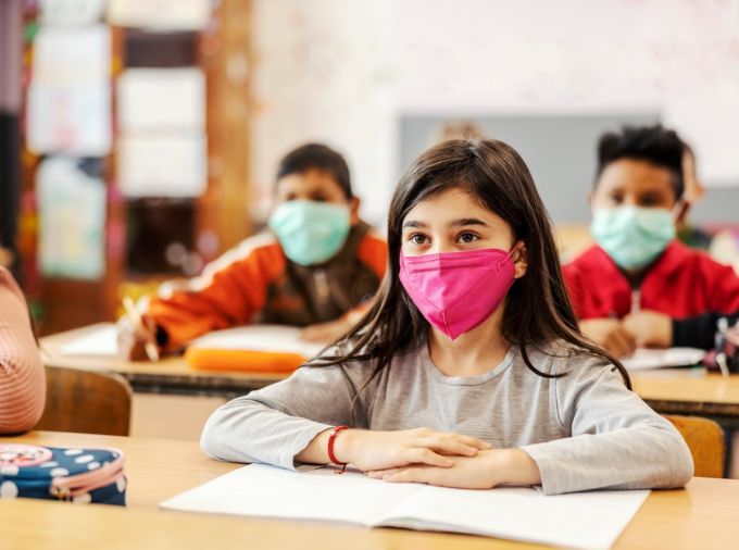 Children at desks at school wearing protective masks.